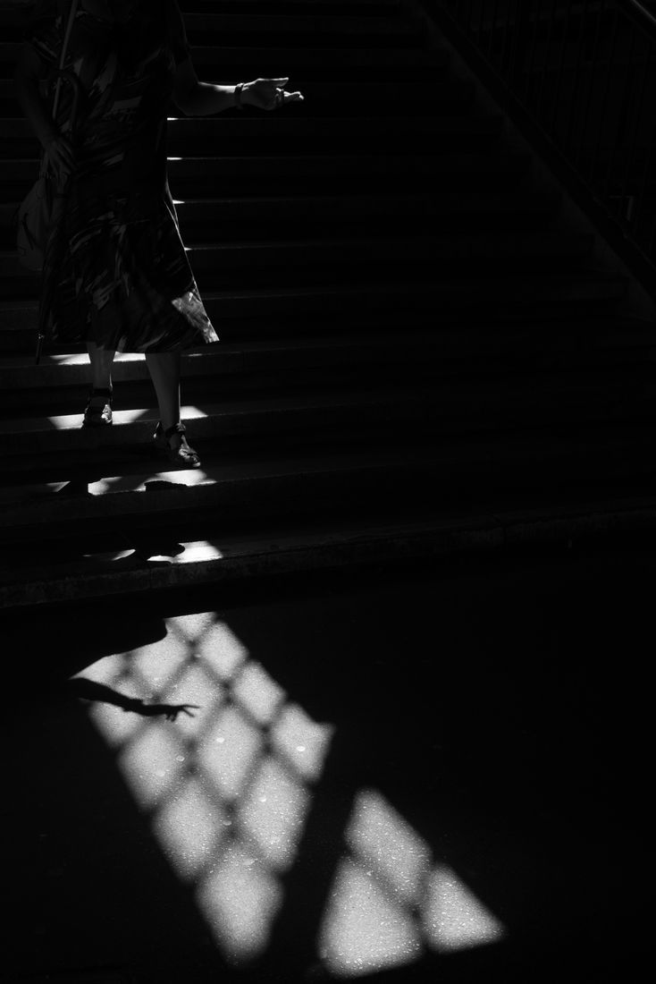 A woman descends dark stairs, her outstretched hand repeated as a shadow in a patch of sunlight